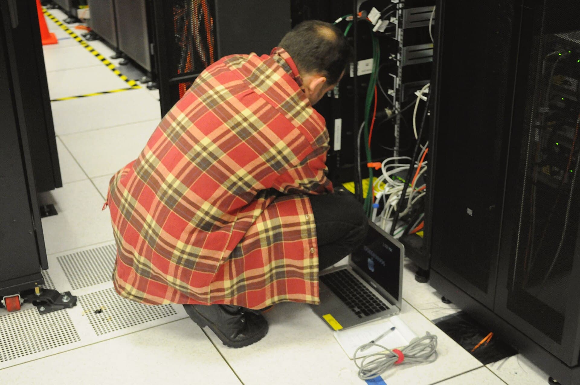 Técnico trabalha com um notebook diante de racks em um data center