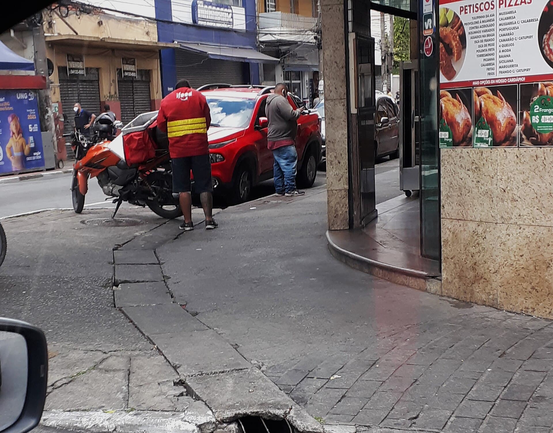Entregador do iFood ao lado de uma motocicleta em uma rua brasileira