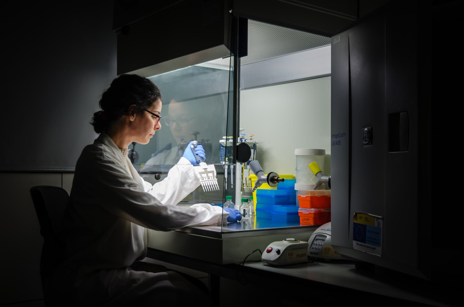 Pesquisadora trabalha diante de equipamentos dentro de uma cabine de laboratório