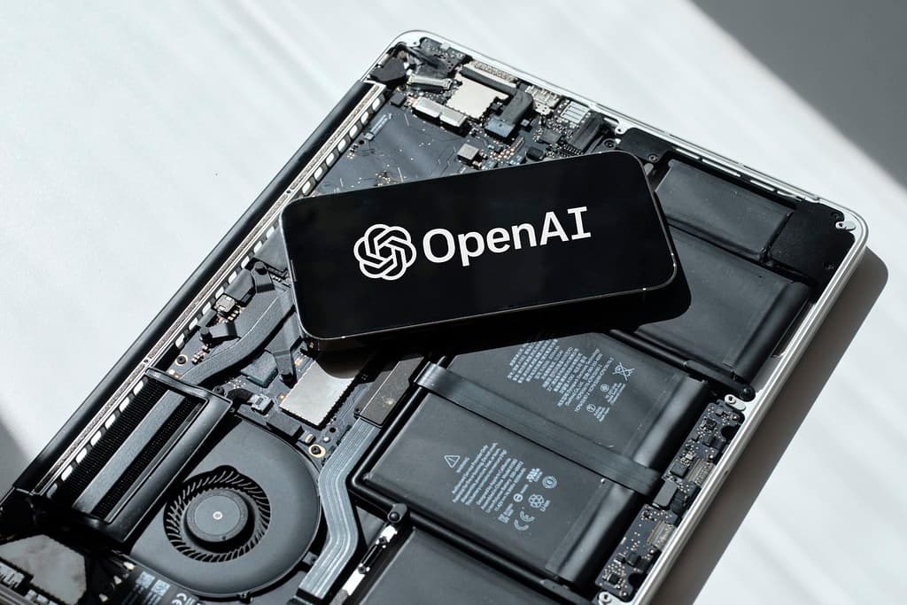 Fotografia de um celular exibindo a marca OpenAI sobre um notebook aberto